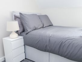 A bedroom with a bed with gray bedding and two pillows next to a white bedside table with a lamp at 9 Beckett Close in Colwyn Bay