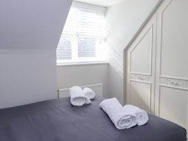 A bedroom with a bed covered in a dark sheet and four rolled white towels beside a window with blinds and built in wardrobes at 9 Beckett Close in Colwyn Bay
