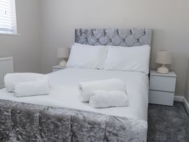 A bedroom with a bed with a tufted headboard two bedside tables with lamps and rolled white towels on the bed at 9 Beckett Close in Colwyn Bay