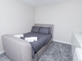 A bedroom with a gray upholstered bed with dark bedding and rolled white towels on it a white dresser and gray carpet at 9 Beckett Close in Colwyn Bay