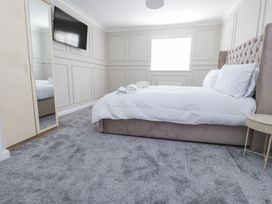 A bedroom with a large bed white bedding a wall-mounted tv a tall mirror wardrobe and a small round table at 9 Beckett Close in Colwyn Bay