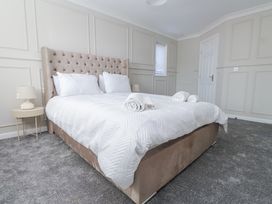 A bedroom with a large bed with white bedding and pillows a beige headboard and nightstands with lamps at 9 Beckett Close in Colwyn Bay