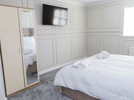 A bedroom with a bed covered with white linens and towels on it a wardrobe with a mirror and a wall-mounted television at 9 Beckett Close in Colwyn Bay