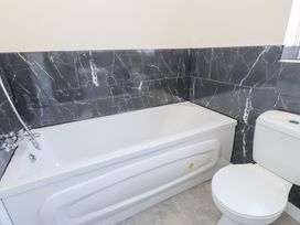 A bathroom with a white bathtub with a shower attachment and a white toilet at 9 Beckett Close in Colwyn Bay