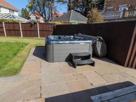 A backyard with a hot tub on a stone patio next to a grass lawn and wooden fence at 9 Beckett Close Colwyn Bay