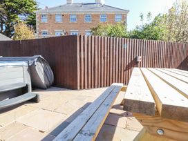 An outdoor patio area with stone paving a wooden picnic table a covered hot tub and a wooden fence at 9 Beckett Close in Colwyn Bay