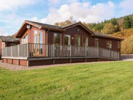 A wooden cabin with a fenced porch surrounded by grass and trees at Crathie Lodge in Banavie near Caol