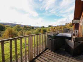 A wooden deck with black outdoor chairs and tables overlooking green fields and trees at Crathie Lodge Banavie near Caol