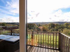 A wooden balcony with glass table and chairs overlooking a green field and trees at Crathie Lodge in Banavie near Caol