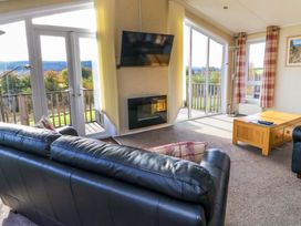 A living room with leather sofas a wooden coffee table a wall-mounted tv and large windows at Crathie Lodge in Banavie near Caol