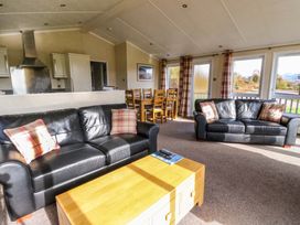 A living room with two black leather sofas a wooden coffee table and a dining table with chairs at Crathie Lodge in Banavie near Caol