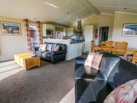 An open living room and kitchen area with black leather sofas a wooden coffee table dining table and kitchen appliances at Crathie Lodge Banavie near Caol