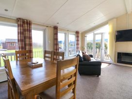 A dining area with wooden table and chairs next to a living area with a sofa and television at Crathie Lodge in Banavie near Caol