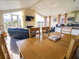 A dining table with chairs in an open living room with sofas a wall mounted TV and kitchen appliances at Crathie Lodge Banavie near Caol
