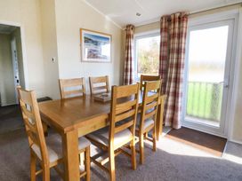 A dining room with a wooden table and six chairs near a window and door with plaid curtains at Crathie Lodge in Banavie near Caol
