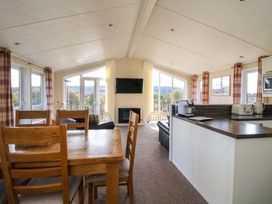 An open plan room with wooden dining table and chairs a kitchen counter with appliances and sofas near windows at Crathie Lodge in Banavie near Caol