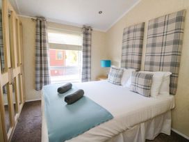 A bedroom with a bed with plaid pillows and headboards next to a window and a blue lamp on a bedside table at Crathie Lodge in Banavie near Caol