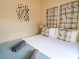 A bedroom with a bed with plaid cushions and headboards two rolled towels on the bed and a lamp on a bedside table at Crathie Lodge in Banavie near Caol