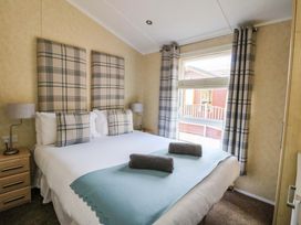 A bedroom with a double bed, plaid headboards and pillows, bedside tables, lamps, and a window with plaid curtains at Crathie Lodge in Banavie near Caol