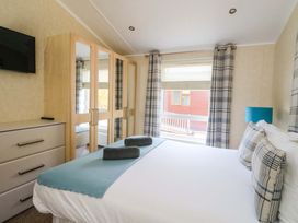 A bedroom with a double bed two rolled towels on it a dresser a wardrobe with mirrors and a window with plaid curtains at Crathie Lodge in Banavie near Caol