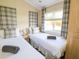 A bedroom with two single beds with plaid headboards and pillows a nightstand with a lamp and a window with plaid curtains at Crathie Lodge Banavie near Caol