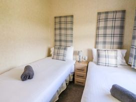 A bedroom with two single beds a bedside table and plaid cushions at Crathie Lodge in Banavie near Caol