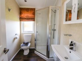 A bathroom with a toilet a shower with glass doors a sink with a mirror cabinet and an orange window blind at Crathie Lodge Banavie near Caol