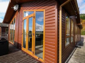 The exterior of a wooden cabin with glass doors and windows and a satellite dish on a deck at Crathie Lodge in Banavie near Caol