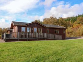 A single story wooden cabin with multiple windows and a fenced porch on a grassy plot at Crathie Lodge in Banavie near Caol