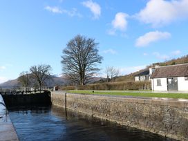 A canal lock with stone walls next to grass and trees with houses and hills in the background at Crathie Lodge in Banavie near Caol