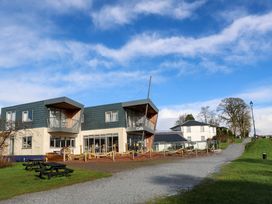 A modern building with balconies and a cafe sign next to a gravel path with picnic tables on a grassy area at Crathie Lodge in Banavie near Caol