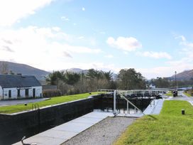 A canal lock system with grassy banks and a small white building near mountains at Crathie Lodge in Banavie near Caol