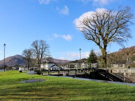 A canal lock with metal railings surrounded by grass trees and houses with mountains in the background at Crathie Lodge Banavie near Caol