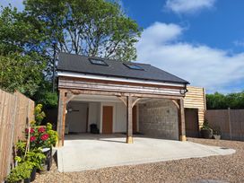 An open wooden garage with two skylights and a concrete floor surrounded by plants and fencing at The Halt in Maiden Newton