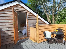 A small outdoor patio with a round table and two chairs next to a wooden house with an open door showing a bedroom at The Halt in Maiden Newton