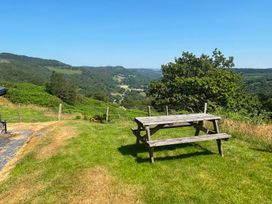 A picnic table on grass with trees and mountains in the background at Ty Siabod, Capel Curig near Betws-Y-Coed