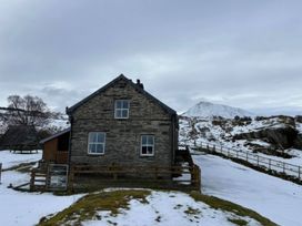 A stone house with snow around and mountains in the background at Ty Siabod in Capel Curig near Betws-Y-Coed