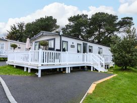 A white static caravan with a ramp and stairs on a paved area surrounded by trees at 117 Crosswinds in Hillway near Bembridge