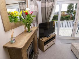 A living room with a wooden fireplace mantel with flowers and reed diffusers a flat screen tv on a wooden stand and sliding glass doors leading to a deck at 117 Crosswinds Hillway near Bembridge