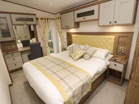 A bedroom with a bed with yellow and plaid bedding a dressing table with a chair built in cupboards and floral curtains at 117 Crosswinds in Hillway near Bembridge