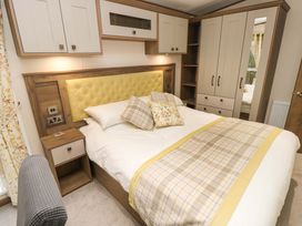 A bedroom with a bed with patterned pillows and throw blanket a wardrobe with mirror and overhead cabinets at 117 Crosswinds in Hillway near Bembridge
