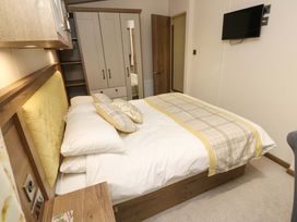 A bedroom with a double bed yellow headboard a wardrobe with mirror and a TV on the wall at 117 Crosswinds Hillway near Bembridge