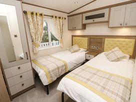 A bedroom with two single beds bedside table wardrobe and window with floral curtains at 117 Crosswinds in Hillway near Bembridge