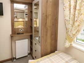 A bedroom corner with a wooden wardrobe with drawers a mirror a radiator and a window with floral curtains at 117 Crosswinds in Hillway near Bembridge