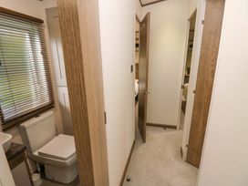A narrow hallway with carpeted floor leading to an open door with visible bedrooms and a bathroom with a toilet and window blinds at 117 Crosswinds Hillway near Bembridge