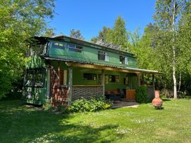 A green double-decker bus converted into a house with a covered porch surrounded by grass and trees at Walter in Wells-Next-The-Sea