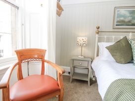 A bedroom with a bed, nightstand, lamp, and chair at 11A High Street in Jedburgh