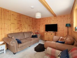 A living room with wooden panel walls two brown sofas a plaid armchair a television on a wooden cabinet a floor lamp and a small rug on the floor at Bradan Lodge in Dalmally