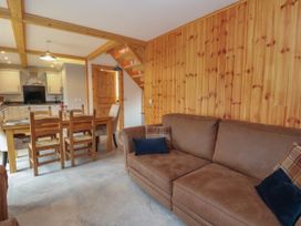 A living room area with a brown sofa and cushions next to a wooden dining table with six chairs and a kitchen in the background at Bradan Lodge Dalmally