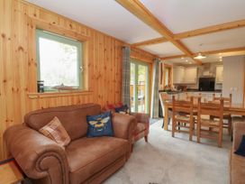 A living area with a leather sofa, armchair, wooden dining table with chairs and a kitchen in the background at Bradan Lodge in Dalmally